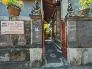 Ein traditionelles balinesisches Tor mit einem Schild für Inten House, inklusive Annehmlichkeiten wie warmer und kalter Dusche, Deckenventilator und Frühstück.
