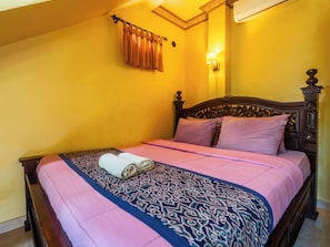 A bed with a patterned bedspread, pillows, and a rolled towel.