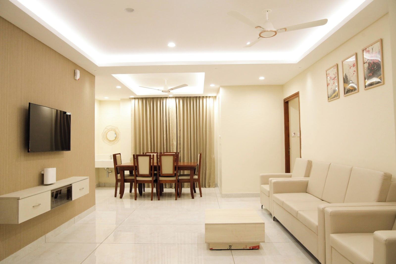 A modern living room with a flat-screen TV, a dining area with a table and chairs, a sofa, and a ceiling fan.