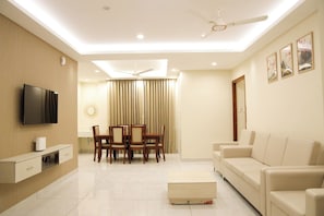 A modern living room with a flat-screen TV, a dining area with a table and chairs, a sofa, and a ceiling fan.