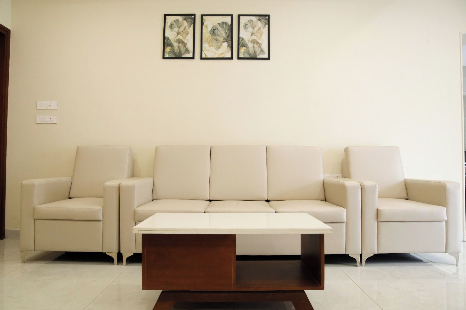 A living room with a beige sofa set, a white coffee table, and two framed artworks on the wall.