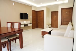A modern living room with a dining table, white sofa, and a TV mounted on the wall.