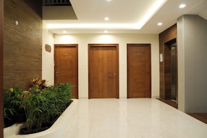 A modern hallway with three wooden doors, a tiled floor, and a planter with plants.