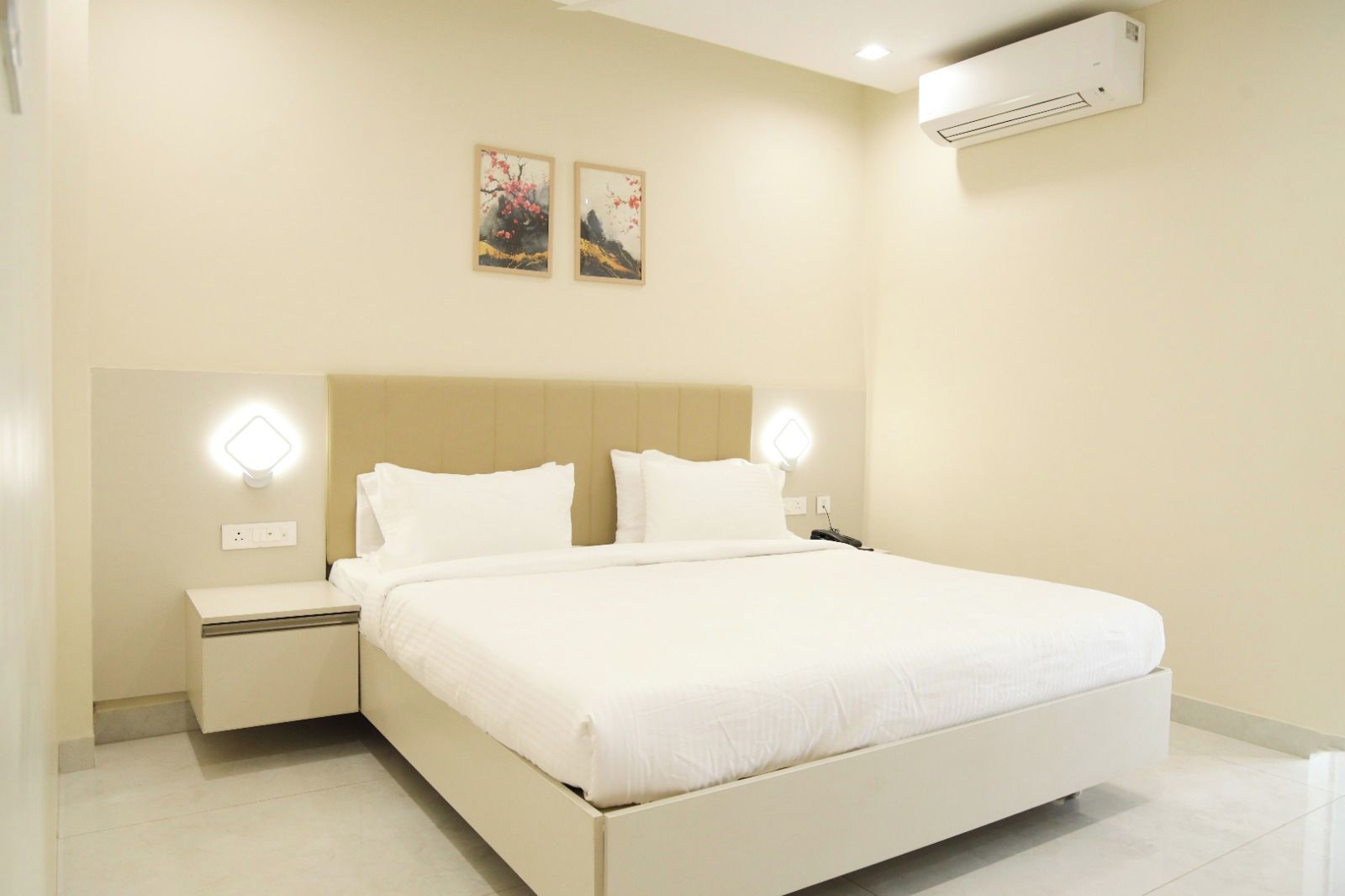 A hotel room with a large bed, bedside tables, wall-mounted air conditioning, and two wall-mounted light fixtures.