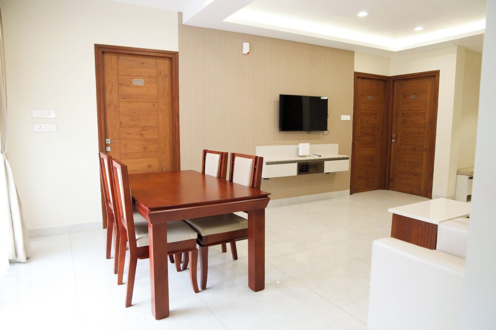 A modern dining area with a wooden table and chairs, a built-in TV, and a kitchenette.