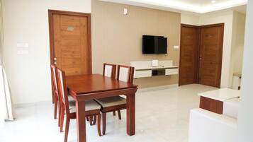 A modern dining area with a wooden table and chairs, a built-in TV, and a kitchenette.