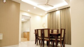 A dining area with a table and chairs, a ceiling fan, and a kitchen in the background. - SS Grandur  (Tiruchirappalli)