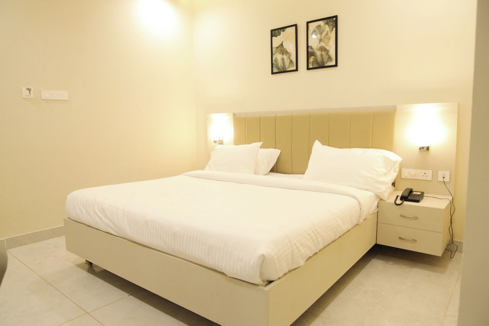 A hotel room with a bed, bedside tables, a telephone, and wall-mounted lights.