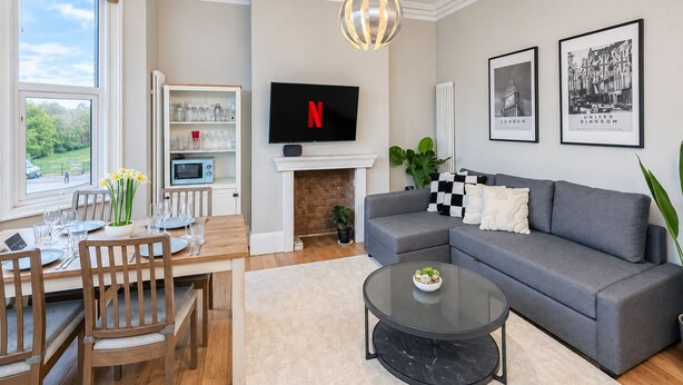 Un salon moderne avec un canapé gris, un téléviseur à écran plat, une cheminée et un coin repas doté de meubles en bois.