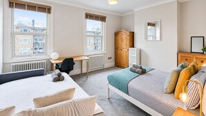 Une chambre avec deux lits, un bureau, une armoire et un radiateur.