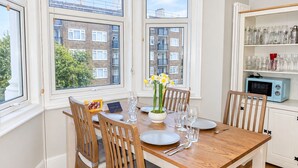 Un coin repas avec une table en bois dressée pour quatre personnes, des chaises, un vase de fleurs et un four à micro-ondes posé sur une étagère.