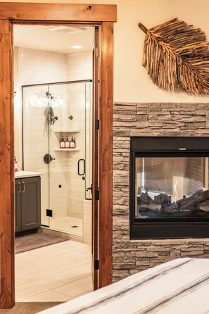 A bathroom with a glass shower enclosure, a stone wall with a fireplace, and a wooden door frame. - Welcome to Seventeen Pines, a stunning Suncadia retreat overlooking Prospector Golf Course’s 17th hole. Enjoy soaring ceilings, a dramatic stone fireplace, private hot tub and beautiful views, all tucked among towering evergreens. (Cle Elum)