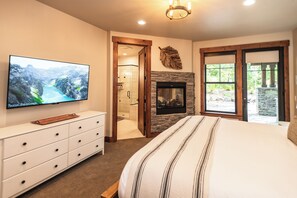 A bedroom with a television, a fireplace, a large bed, and a view of the outdoors through a glass door. - Welcome to Seventeen Pines, a stunning Suncadia retreat overlooking Prospector Golf Course’s 17th hole. Enjoy soaring ceilings, a dramatic stone fireplace, private hot tub and beautiful views, all tucked among towering evergreens. (Cle Elum)