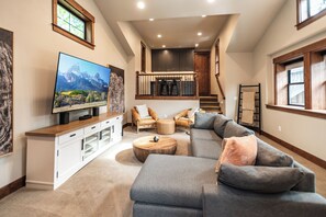 A spacious living room with a large sectional sofa, a flat-screen TV, and a wooden coffee table. - Welcome to Seventeen Pines, a stunning Suncadia retreat overlooking Prospector Golf Course’s 17th hole. Enjoy soaring ceilings, a dramatic stone fireplace, private hot tub and beautiful views, all tucked among towering evergreens. (Cle Elum)