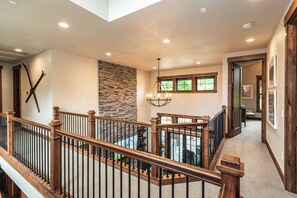 A spacious interior with a high ceiling, a stone accent wall, and a wooden staircase with a railing. - Welcome to Seventeen Pines, a stunning Suncadia retreat overlooking Prospector Golf Course’s 17th hole. Enjoy soaring ceilings, a dramatic stone fireplace, private hot tub and beautiful views, all tucked among towering evergreens. (Cle Elum)