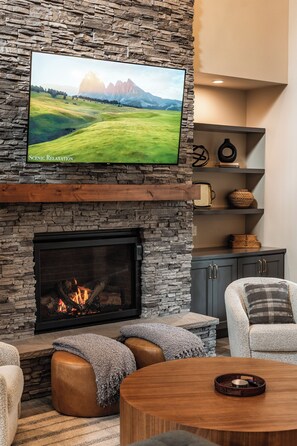 A living room with a stone fireplace, a mounted television, and a cozy seating area. - Welcome to Seventeen Pines, a stunning Suncadia retreat overlooking Prospector Golf Course’s 17th hole. Enjoy soaring ceilings, a dramatic stone fireplace, private hot tub and beautiful views, all tucked among towering evergreens. (Cle Elum)