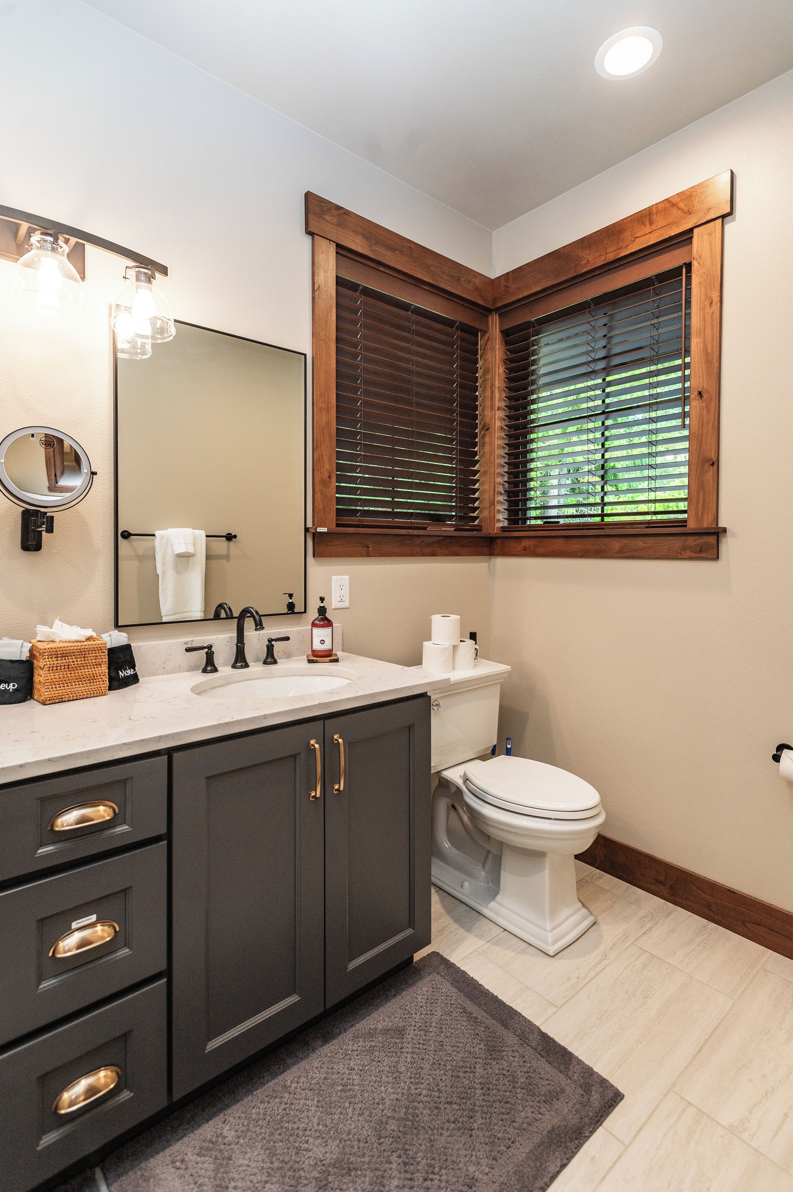 A bathroom with a vanity, mirror, towel rack, and a window with blinds.
