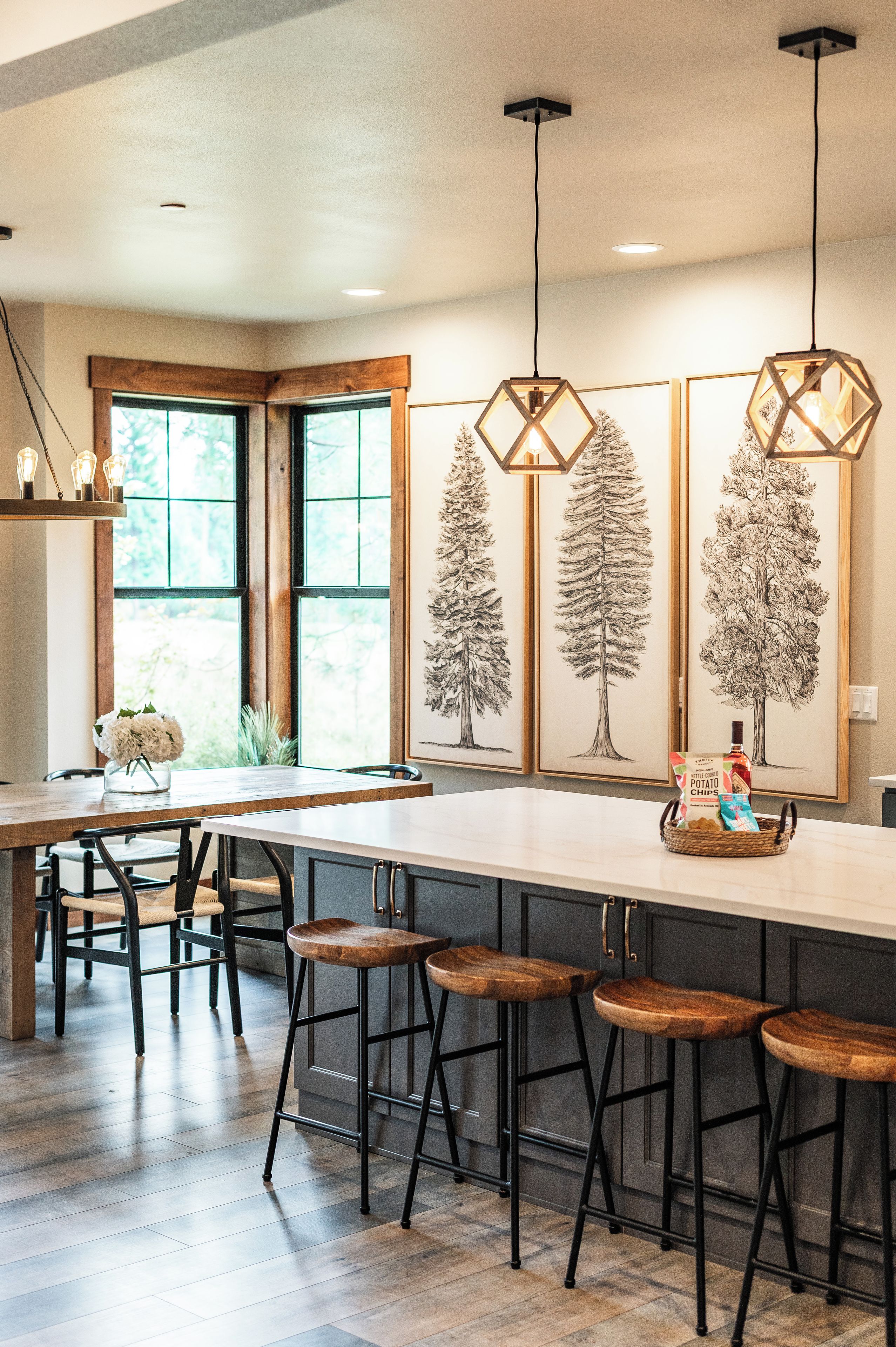 A modern kitchen with a central island, bar stools, pendant lighting, and framed botanical prints on the wall.