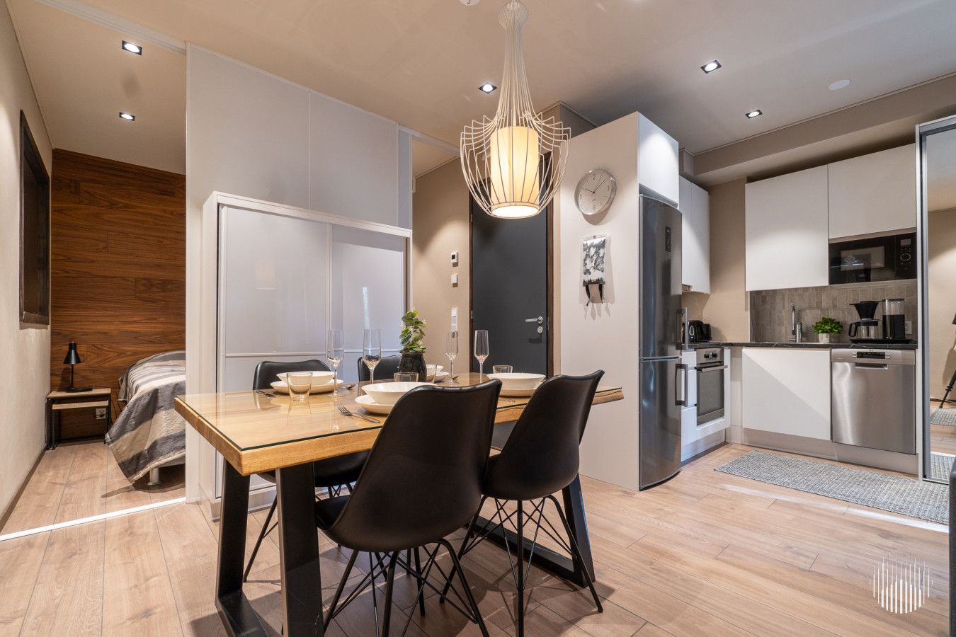 A modern kitchen with stainless steel appliances, a dining area with a wooden table and black chairs, and a visible clock on the wall.