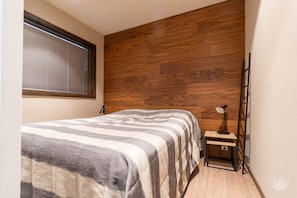 A bedroom with a bed, a nightstand, a lamp, a window with blinds, and a wooden wall panel. - Hiihtäjänkuja 2 B4 by Holiday in Lapland (Levi)