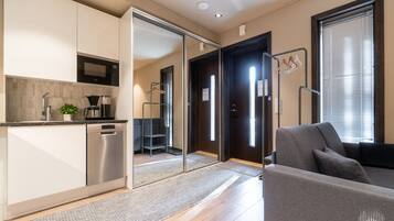 A modern kitchen with a built-in microwave, a coffee maker, and a plant. There is a sliding door leading to a living area with a sofa and a window.