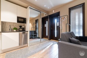 A modern kitchen with a built-in microwave, a coffee maker, and a plant. There is a sliding door leading to a living area with a sofa and a window. - Hiihtäjänkuja 2 B4 by Holiday in Lapland (Levi)