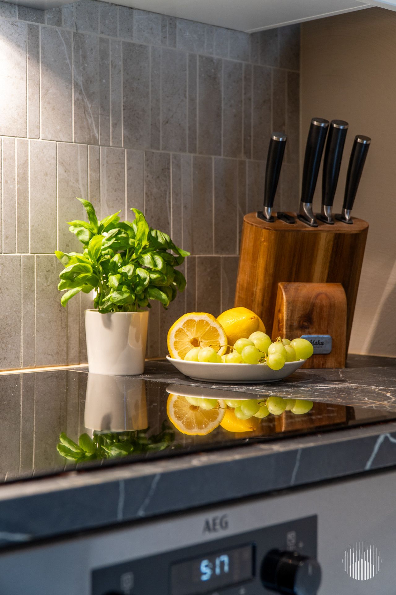 A kitchen counter with a potted plant, a plate of lemons and grapes, and a knife block.