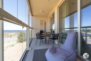 Ein Balkon mit Tisch und Stühlen, einer gepolsterten Sitzecke und Meerblick.