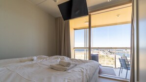 A hotel room with a bed, a TV mounted on the wall, and a balcony with a view of the beach. - Keskuskarintie 120 by Holiday in Kalajoki (Kalajoki)