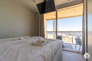 Ein Hotelzimmer mit Bett, Wandfernseher und Balkon mit Meerblick.