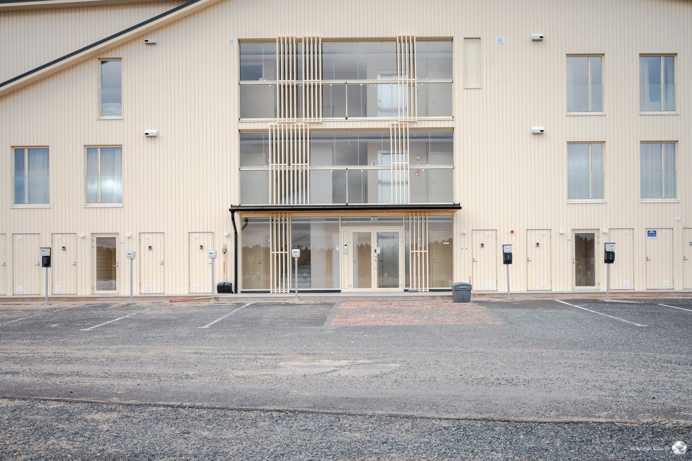 Monikerroksinen rakennus, jossa on keskeinen sisäänkäynti, useita ikkunoita ja pysäköintialue edessä.