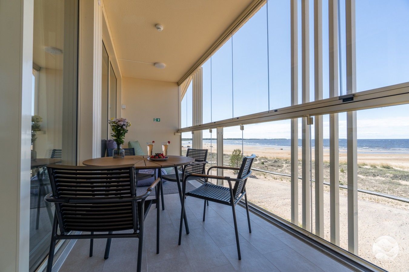 A balcony with a table and chairs, overlooking a beach.