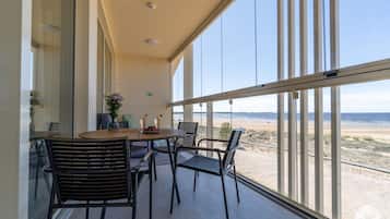 A balcony with a table and chairs, overlooking a beach.