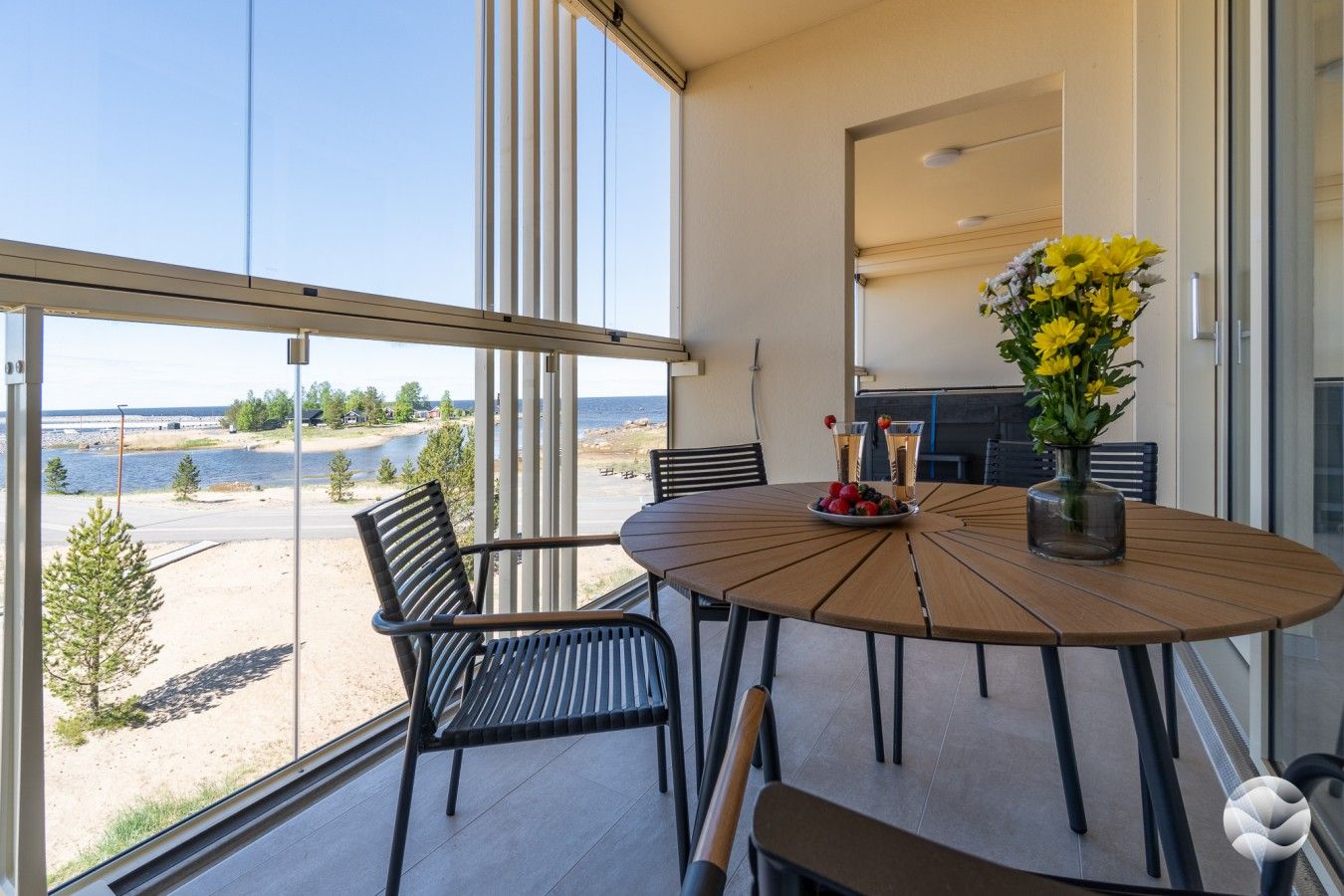 Un balcon avec une table et des chaises, un vase rempli de fleurs jaunes et une vue sur la mer.