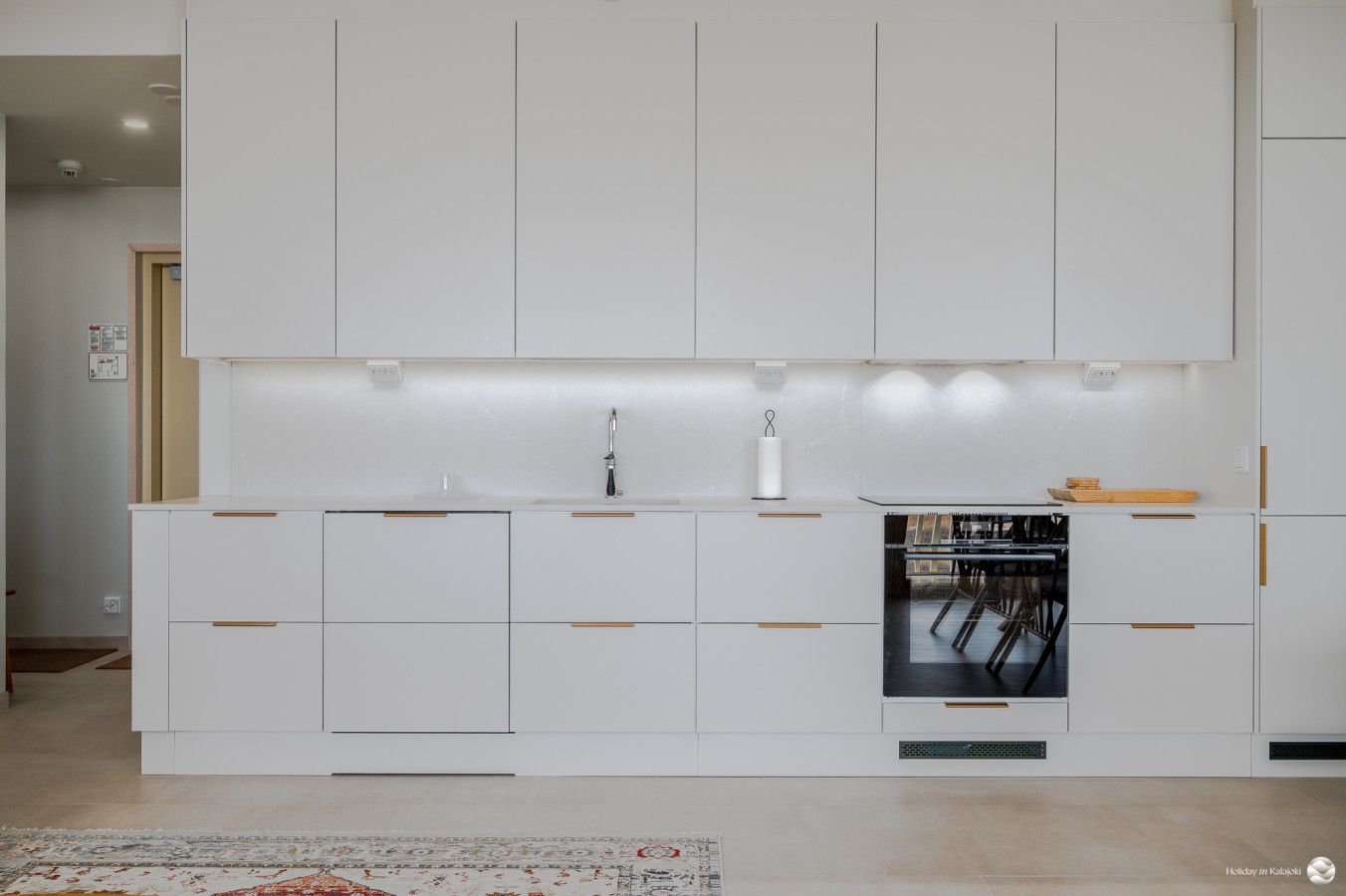 A modern kitchen with white cabinetry, a built-in oven, and a dining area with chairs.