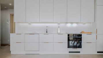 A modern kitchen with white cabinetry, a built-in oven, and a dining area with chairs.