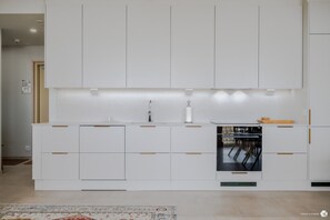 A modern kitchen with white cabinetry, a built-in oven, and a dining area with chairs.