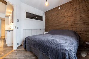 Ein Schlafzimmer mit einem Bett, einem Fenster, Holzvertäfelung an den Wänden und einer Küchenzeile.