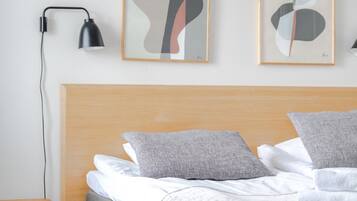 A hotel room with a wooden headboard, a bed with grey bedding, two abstract wall art pieces, a black desk lamp, and a small wooden side table.
