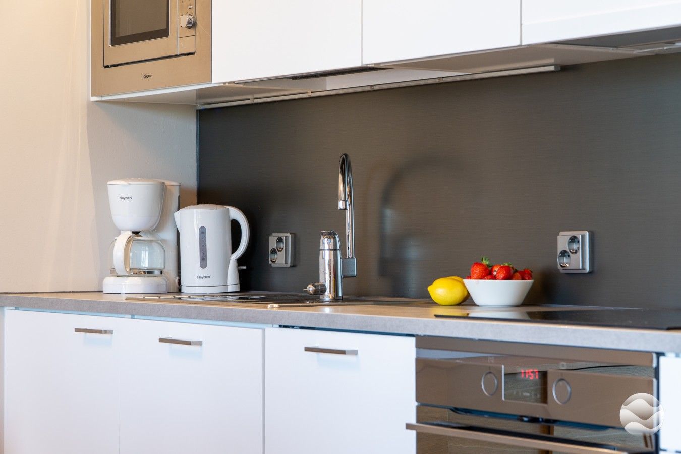 A modern kitchen with a coffee maker, kettle, and fruit bowl on the counter.