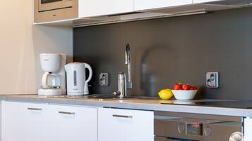 A modern kitchen with a coffee maker, kettle, and fruit bowl on the counter.