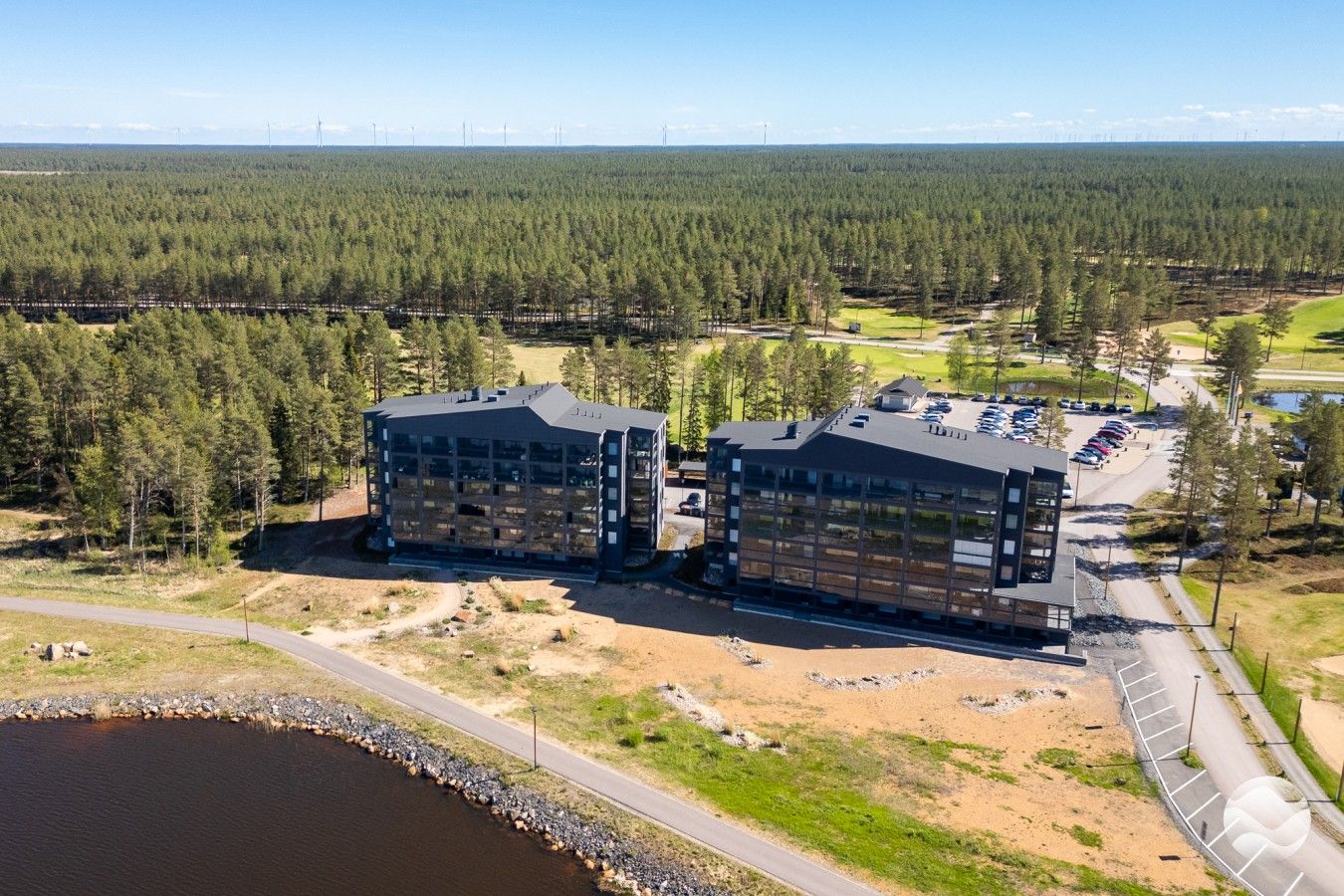Moderni rakennus, jossa on suuri pysäköintialue ja näkymä metsäiselle maisemalle.