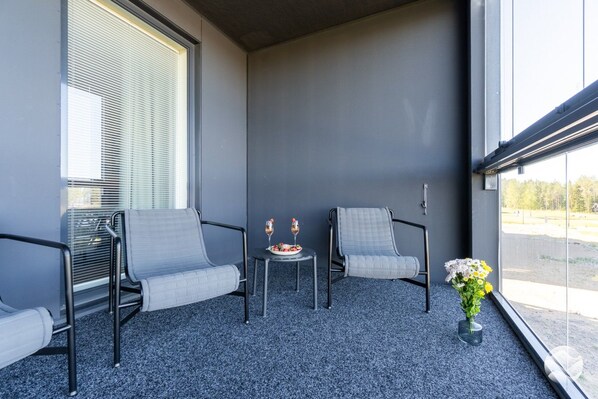 A balcony with two chairs, a small table, and a vase of flowers.