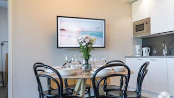 Un comedor con una mesa preparada para cuatro, un jarrón de flores y un cuadro colgado sobre la mesa.