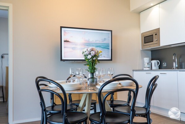 Un coin repas avec une table dressée pour quatre personnes, un vase de fleurs et un tableau encadré au-dessus de la table.