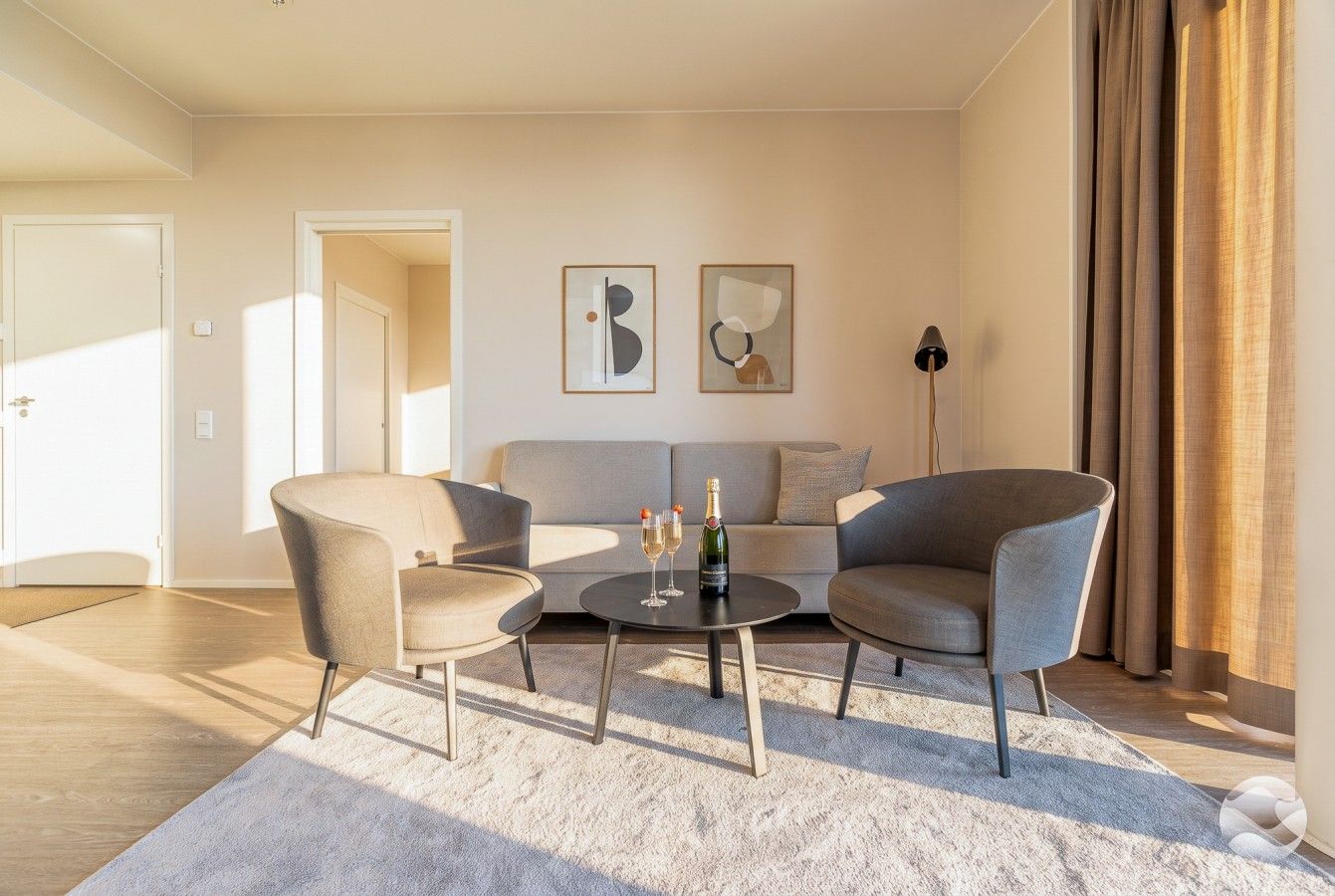 Ein modernes Wohnzimmer mit einer Couch, zwei Sesseln, einem Couchtisch und Kunstwerken an der Wand.