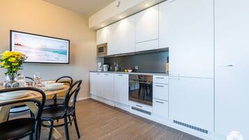 Una cocina moderna con armarios blancos, un comedor con una mesa para dos personas y un cuadro en la pared.