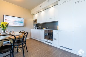 Une cuisine moderne avec des meubles blancs, un coin repas avec une table dressée pour deux personnes, et un tableau accroché au mur.