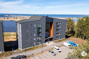 A modern building with multiple floors, a parking lot, and a view of the sea.