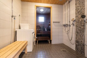 A bathroom with a shower, a bench, a washing machine, and a tiled floor. - SanAlppi 7 by Holiday in Lapland (Levi)